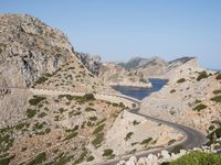 two vehicles driving on the narrow highway in front of the ocean near a cliff formation