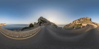 a panorama view of a curved road by the sea under blue skies with some clouds