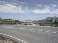 a man rides a skateboard on the side of an empty road on a mountain side