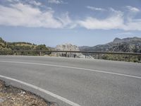 a man rides a skateboard on the side of an empty road on a mountain side