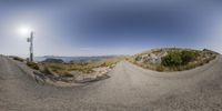 a panorama fish eye shot shows a view of the horizon over a gravel road, some grass, and a telephone pole