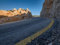 an empty mountain road running along it's side by a cliff wall at sunset