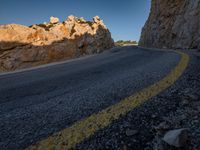 an empty mountain road running along it's side by a cliff wall at sunset