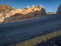 an empty mountain road running along it's side by a cliff wall at sunset