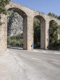 an old bridge over a narrow road near the mountains in spain on a clear day