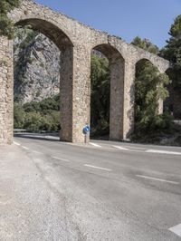 an old bridge over a narrow road near the mountains in spain on a clear day