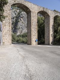 an old bridge over a narrow road near the mountains in spain on a clear day