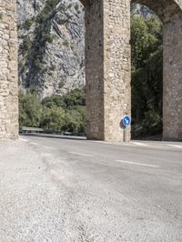 an old bridge over a narrow road near the mountains in spain on a clear day