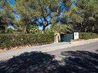 a small white gate sitting on the side of a road near some trees and bushes