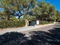 a small white gate sitting on the side of a road near some trees and bushes