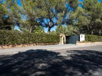 a small white gate sitting on the side of a road near some trees and bushes