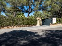 a small white gate sitting on the side of a road near some trees and bushes