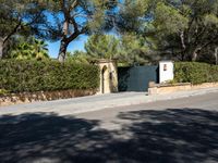 a small white gate sitting on the side of a road near some trees and bushes