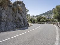 a curved road on a mountain side with steep cliffs in the background and a bike rider wearing a black helmet