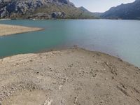 a mountain area that has water and rocks on the beach near the shore of a lake