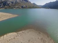 a mountain area that has water and rocks on the beach near the shore of a lake