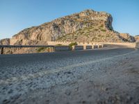 the motorcycle is parked at the edge of the stone road near a mountain and sky