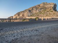 the motorcycle is parked at the edge of the stone road near a mountain and sky