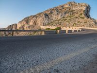 the motorcycle is parked at the edge of the stone road near a mountain and sky