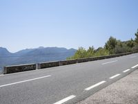 a mountain range next to a road with trees and mountains on one side and a person in the other riding on the road