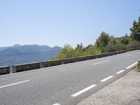 a mountain range next to a road with trees and mountains on one side and a person in the other riding on the road