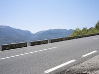 a mountain range next to a road with trees and mountains on one side and a person in the other riding on the road