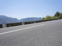 a mountain range next to a road with trees and mountains on one side and a person in the other riding on the road