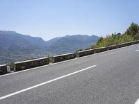 a mountain range next to a road with trees and mountains on one side and a person in the other riding on the road