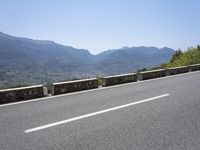 a mountain range next to a road with trees and mountains on one side and a person in the other riding on the road