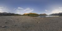 a panorama of the landscape of a mountain side lake and rocky shore line with mountains in the background