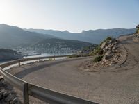 an empty road with many curves going over the mountain side and buildings in the background