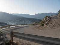 an empty road with many curves going over the mountain side and buildings in the background