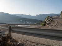 an empty road with many curves going over the mountain side and buildings in the background