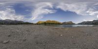 a panorama photo of a lake, mountain, and sky in a cloudy blue sky