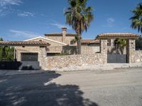 a large house with two cars parked outside it and a palm tree by the side of the road