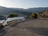 a bench on a road overlooking the water and mountains and trees that are on the edge of the road