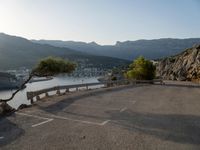 a bench on a road overlooking the water and mountains and trees that are on the edge of the road