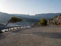 a bench on a road overlooking the water and mountains and trees that are on the edge of the road