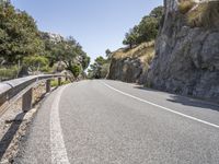 a motorcycle is traveling down the mountain pass of a steep cliff lined road with bushes, grass and trees