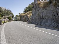 a motorcycle is traveling down the mountain pass of a steep cliff lined road with bushes, grass and trees