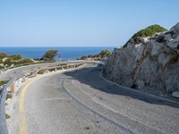 a paved road that passes over the sea and cliffs, near a bench and car