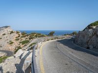 a paved road that passes over the sea and cliffs, near a bench and car