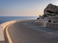 a scenic road stretches into the ocean from the beach with an arched wall surrounding it