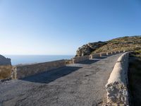 a paved stone walkway with an arch on the side of it with sea views in the distance