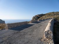 a paved stone walkway with an arch on the side of it with sea views in the distance