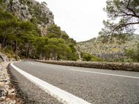 a road is going past mountains with rocks on both sides of the roads and there are trees in the foreground