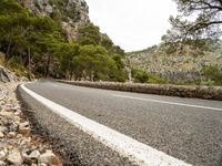 a road is going past mountains with rocks on both sides of the roads and there are trees in the foreground