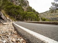 a road is going past mountains with rocks on both sides of the roads and there are trees in the foreground