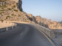 a lone motorcycle travels down an empty road near the seafront on the edge of a cliff