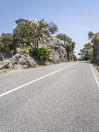 a man riding a motorcycle down the middle of a road with large rocks in the background